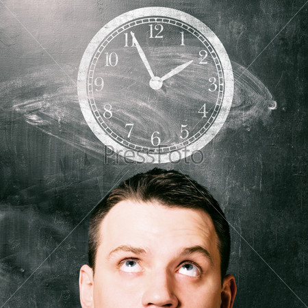 time. man is looking up at clock with chalk board behind him