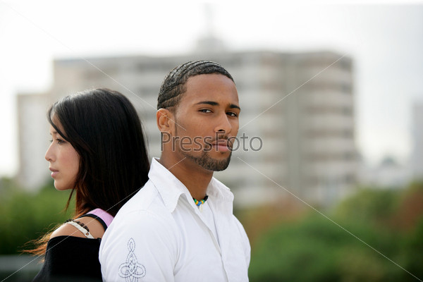 Young couple standing back-to-back on the outskirts of a city, stock photo