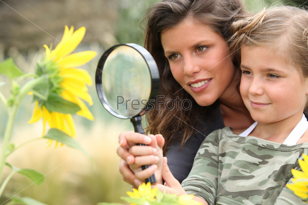 Young mum and daughter looking at a sunflower through a magnifying glass