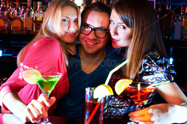 Portrait of pretty girls embracing happy guy and looking at camera at party, stock photo