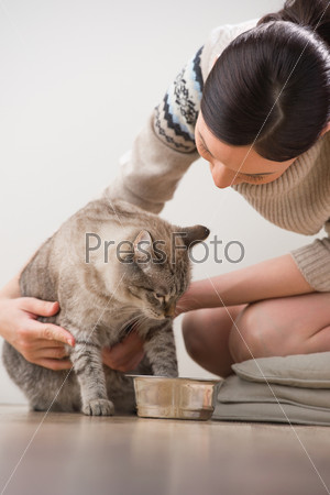 Beautiful young woman feeding her cat at home