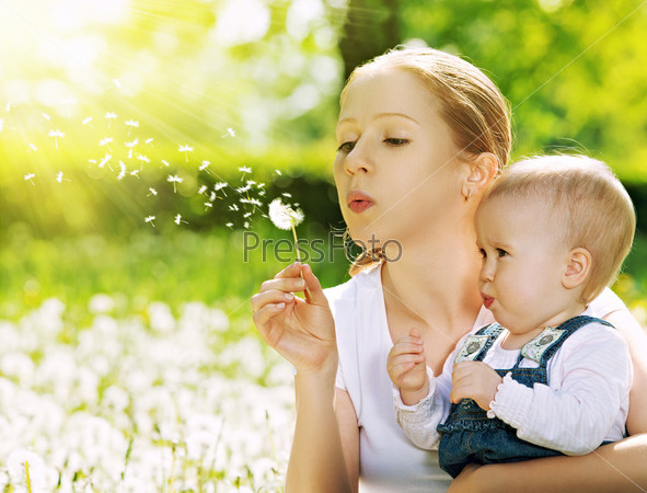 Happy family. Mother and baby girl blowing on a dandelion flower