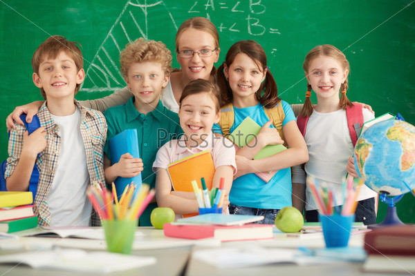 Portrait of cute schoolchildren and their teacher on background of blackboard