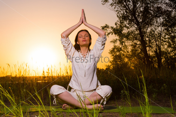 Yoga woman during sunset meditating against the sun outdoors