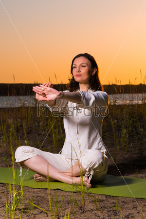 Beautiful young woman doing yoga sitting near the lake during sunset