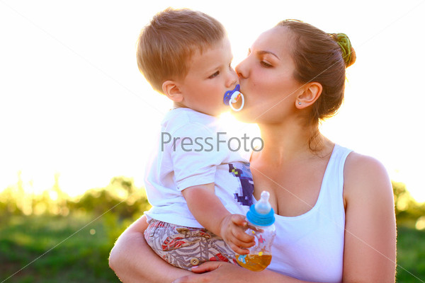 Mother kissing her son on  background of green trees