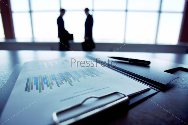 Close-up of a financial report with the silhouettes of business people in the background