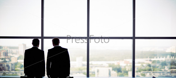Silhouettes of two businessmen standing by the window