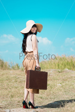Full-length portrait of a young lady with a vintage suitcase in hands