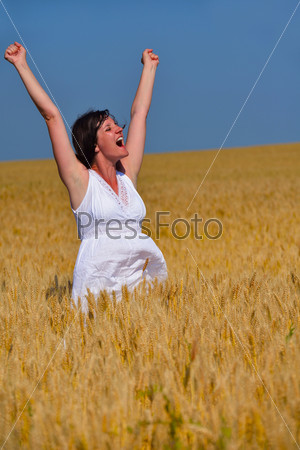 Young woman standing jumping and running on a wheat field\
with blue sky the background at summer day representing healthy\
life and agriculture concept