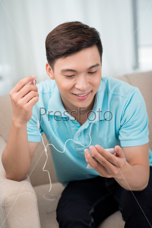 Vertical image of a smiling guy enjoying cool music on his smart phone