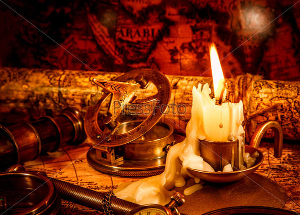 Vintage compass, magnifying glass, pocket watch, spyglass lie on an old ancient map with a lit candle. Vintage still life.