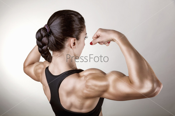 Athletic young woman showing muscles of the back and hands on a gray background, stock photo