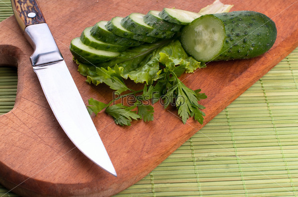 Three cucumbers and the knife on carving board.