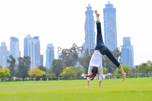 pretty healthy young woman jump and exercise fitness on grass\
in green park with city in background