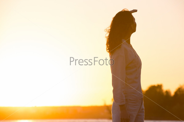Young and beautiful woman in sunset light looking far away. Photo from behind