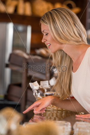 Positive young woman at the bakery store choosing what she wants to by and placing order to seller