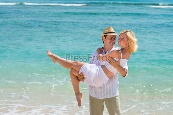 Honeymooner couple. Happy young man carry woman. Couple enjoying at beach with blue sea on background.