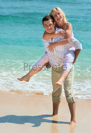 Happy young man carry woman. Couple enjoying at beach with blue sea on background.