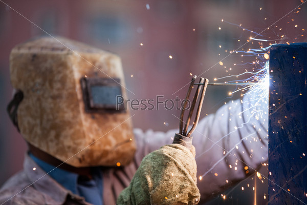 Электросварщик в защитной маске сваривает металлоконструкцию