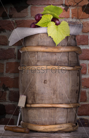 Ripe grapes on a wooden vintage barrel with corkscrew against grunge brick wall background