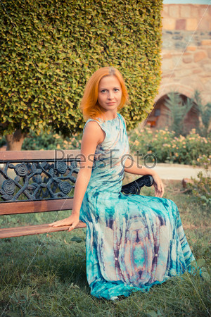 Young red woman wearing long dress sitting on a bench