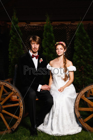 the bride and groom sit on the ancient cart