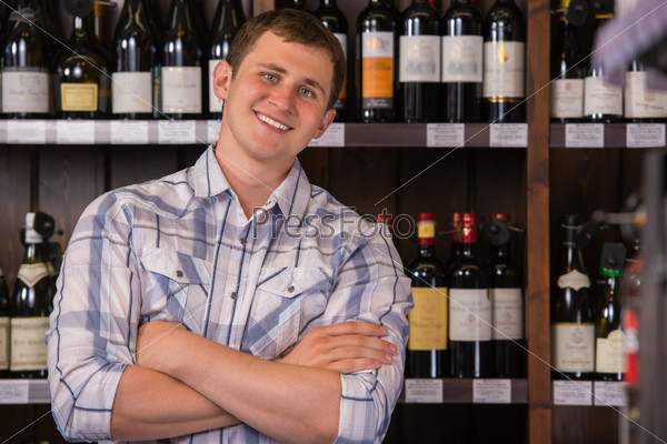 Portrait of confident male holding hands folded with a selection of wines in the background