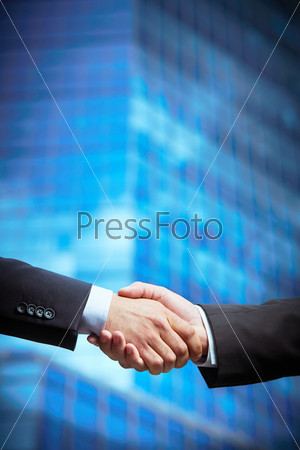 Vertical image of entrepreneurs hands concluding a deal with a skyscraper in the background