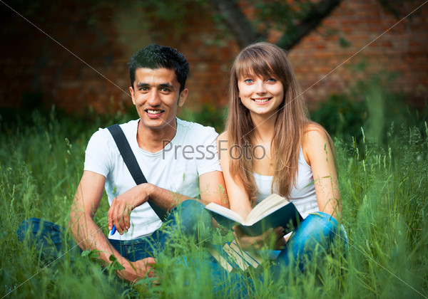 Two students guy and girl studying in park on grass with book outdoors, stock photo