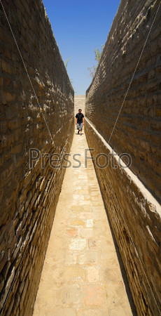 Person walking by the narrow walkway between two brick walls in old asian jailhouse museum