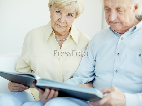 Portrait of a candid senior woman with book looking at camera with her husband near by