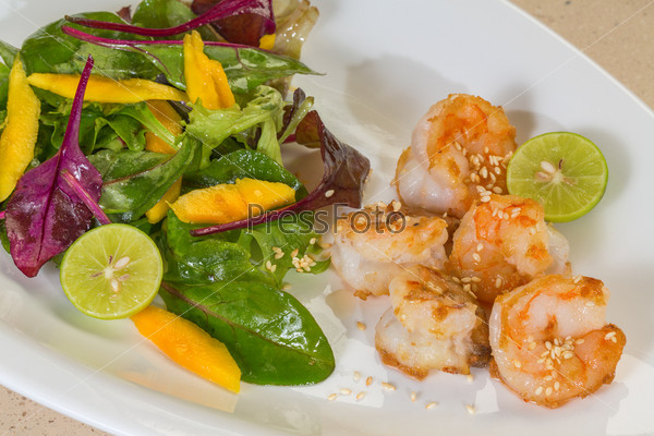 Fresh salad with fried shrimps, variety of salad leafs, mango, lime, and toasted sesame