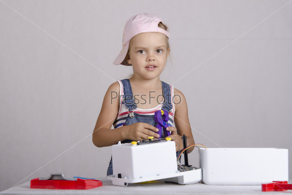 Girl playing in the repairer and repairs toy microwave. A girl Holds the pliers in which clamped nut and looks in a frame