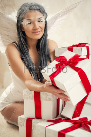 Beautiful young woman as angel with heap of gift boxes posing indoors