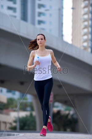 Running in city park. Woman runner outside jogging at morning with Dubai urban scene in background, stock photo