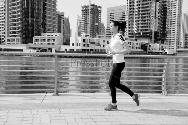Running in city park. Woman runner outside jogging at morning with Dubai urban scene in background, stock photo
