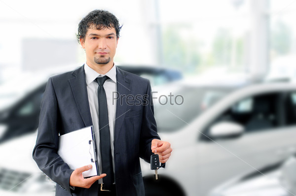 Handsome young classic car salesman standing at the dealership holding a key for a car