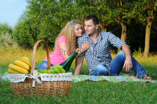Loving young couple enjoying their intimate picnic with a basket of fruit and wine