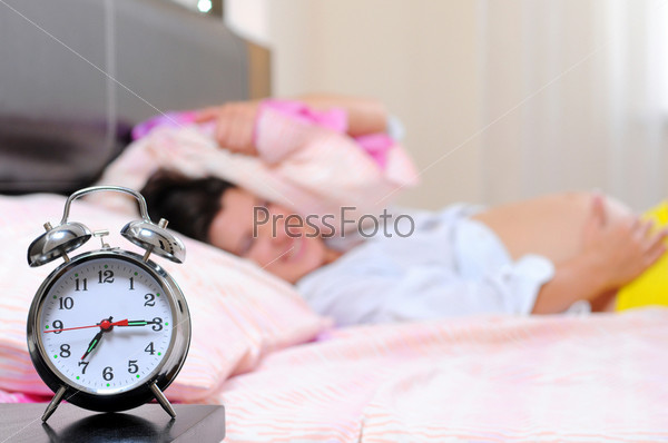 beautiful young pregnant woman with alarm clock in bed at home