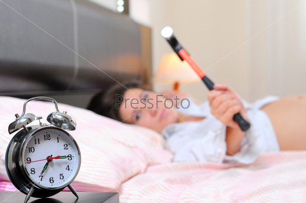 beautiful young pregnant woman with alarm clock in bed at home