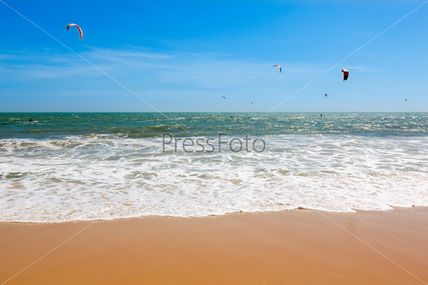 sea, waves on the beach with yellow sand against the blue sky and kiters