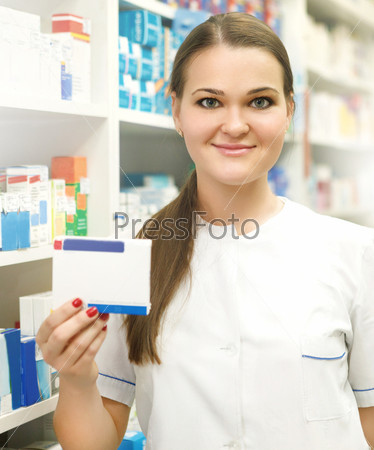 Portrait of young female pharmacist showing medicine box at pharmacy counter