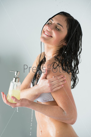 Beautiful girl showering. Holding glass bottle with shower gel and washing herself while water is splashing