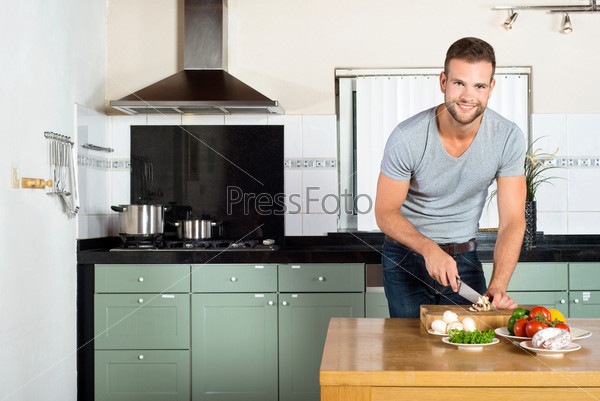 Portrait of handsome smiling man cutting vegetables at kitchen counter