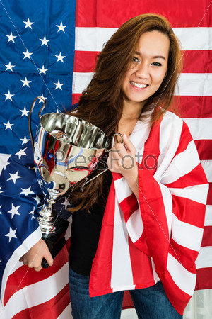 Portrait of happy young sportswoman holding trophy while standing against North American flag