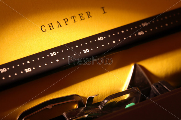 Closeup of electrical typewriter with yellow paper sheet. Inscription Chapter One on paper