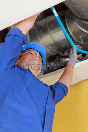 Plumber holding a blue flexible pipe under some air ducts
