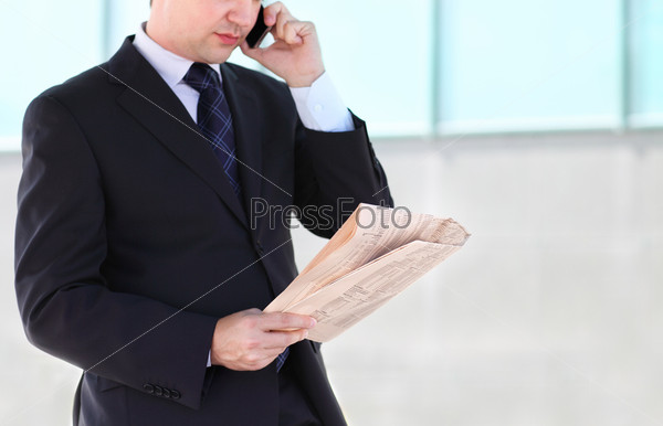 Close up of the hands of the businessman with a newspaper talking by mobile phone. Outdoors