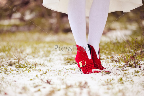 feet of the girl in red shoes and white stockings stand on snow